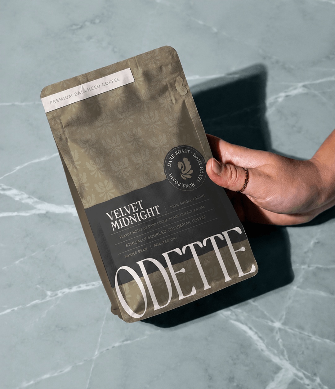 Hand holding a custom designed coffee bag for Odette with strong, elegant branding on light blue marble table.